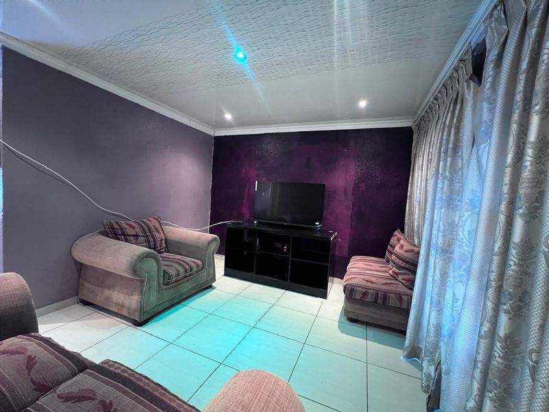 A living room featuring tiled flooring, recessed downlighting, and a textured ceiling. The space would benefit from a fresh coat of paint and cable management.