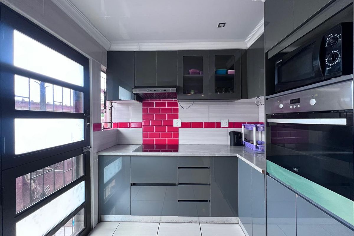Modern kitchen featuring grey high-gloss cabinetry, pink subway tile backsplash, integrated AEG oven, built-in microwave, and sleek stone-look countertops.