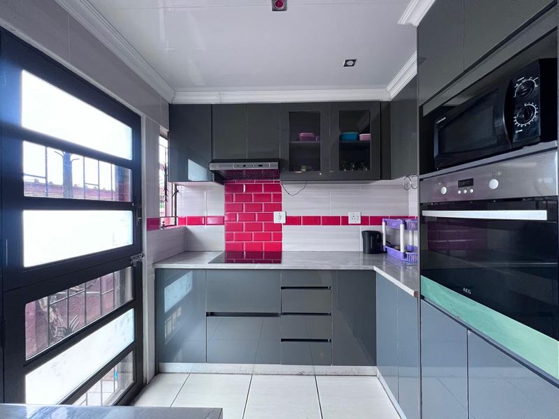 Modern kitchen featuring grey high-gloss cabinetry, pink subway tile backsplash, integrated AEG oven, built-in microwave, and sleek stone-look countertops.