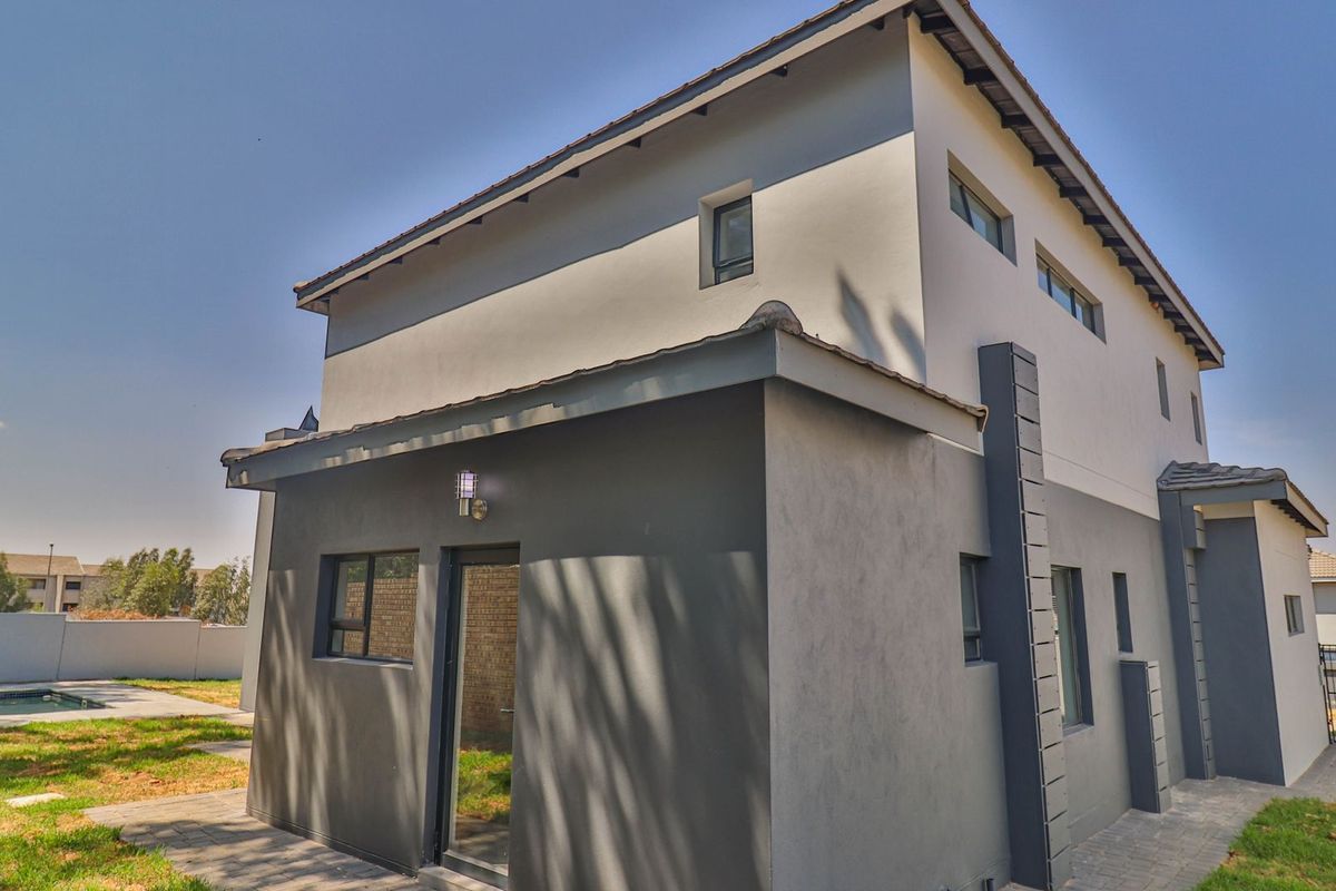 A modern two-story residential exterior featuring a clean plastered facade, tiled roof, and paved walkway leading to the rear garden area.