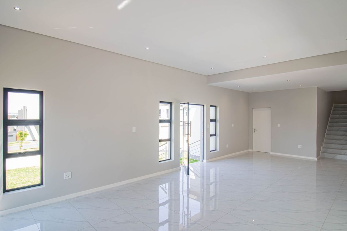 Spacious, modern open-plan living area featuring polished porcelain tile flooring, recessed downlighting, and a contemporary staircase with a glass balustrade.