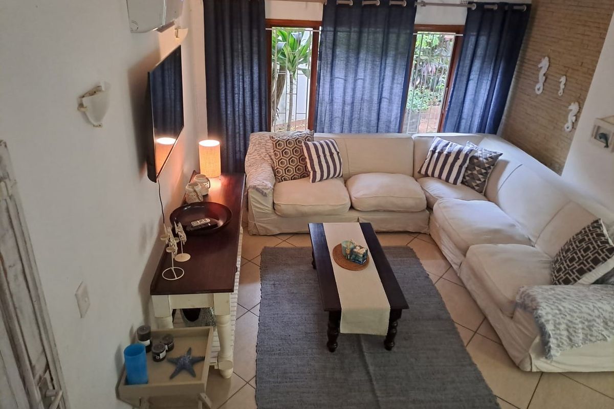 A cozy living room featuring tiled flooring, a brick feature wall, and large windows providing natural light and garden views.