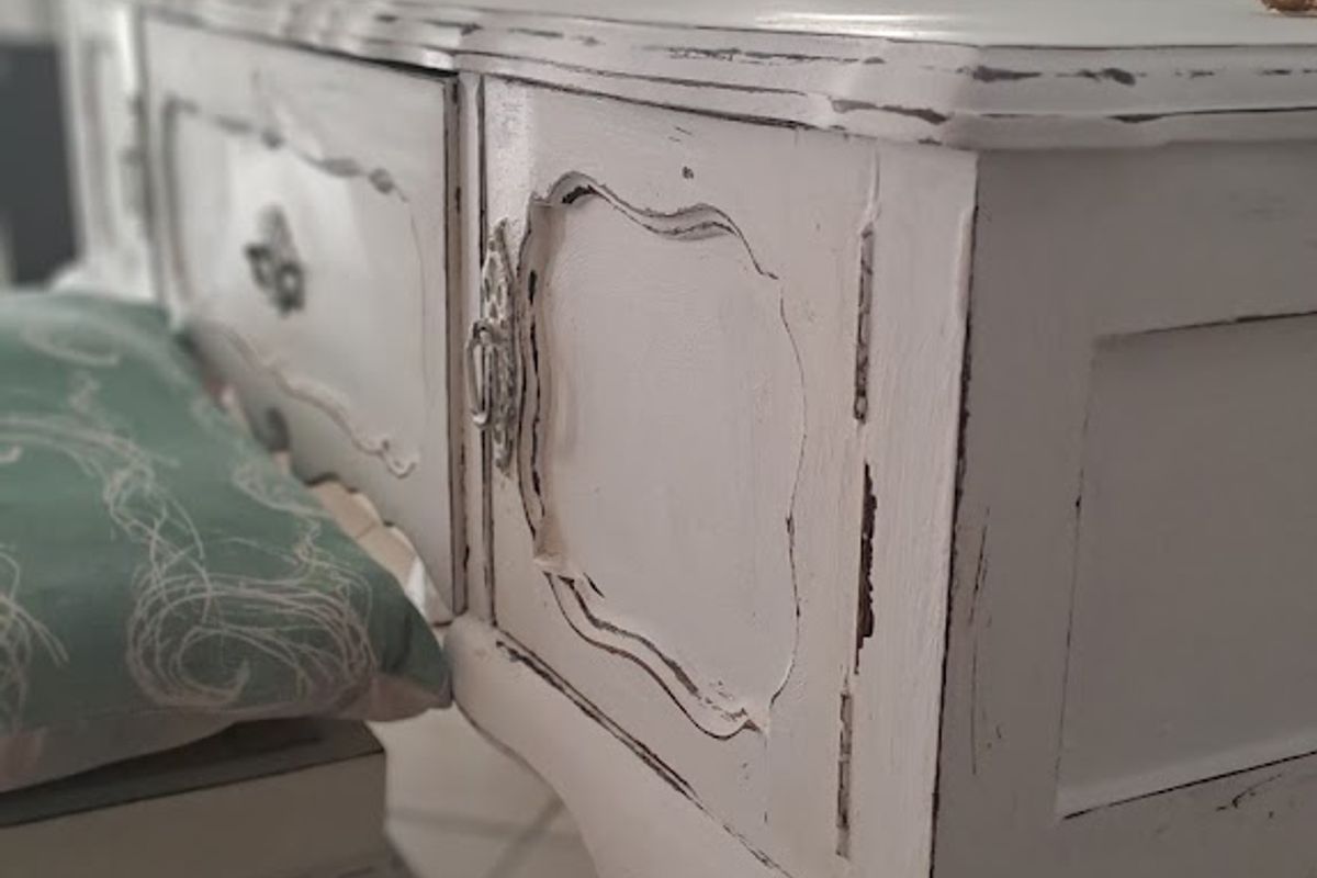 A close-up view of a vintage-style vanity table featuring distressed white paint finish and ornate detailing.