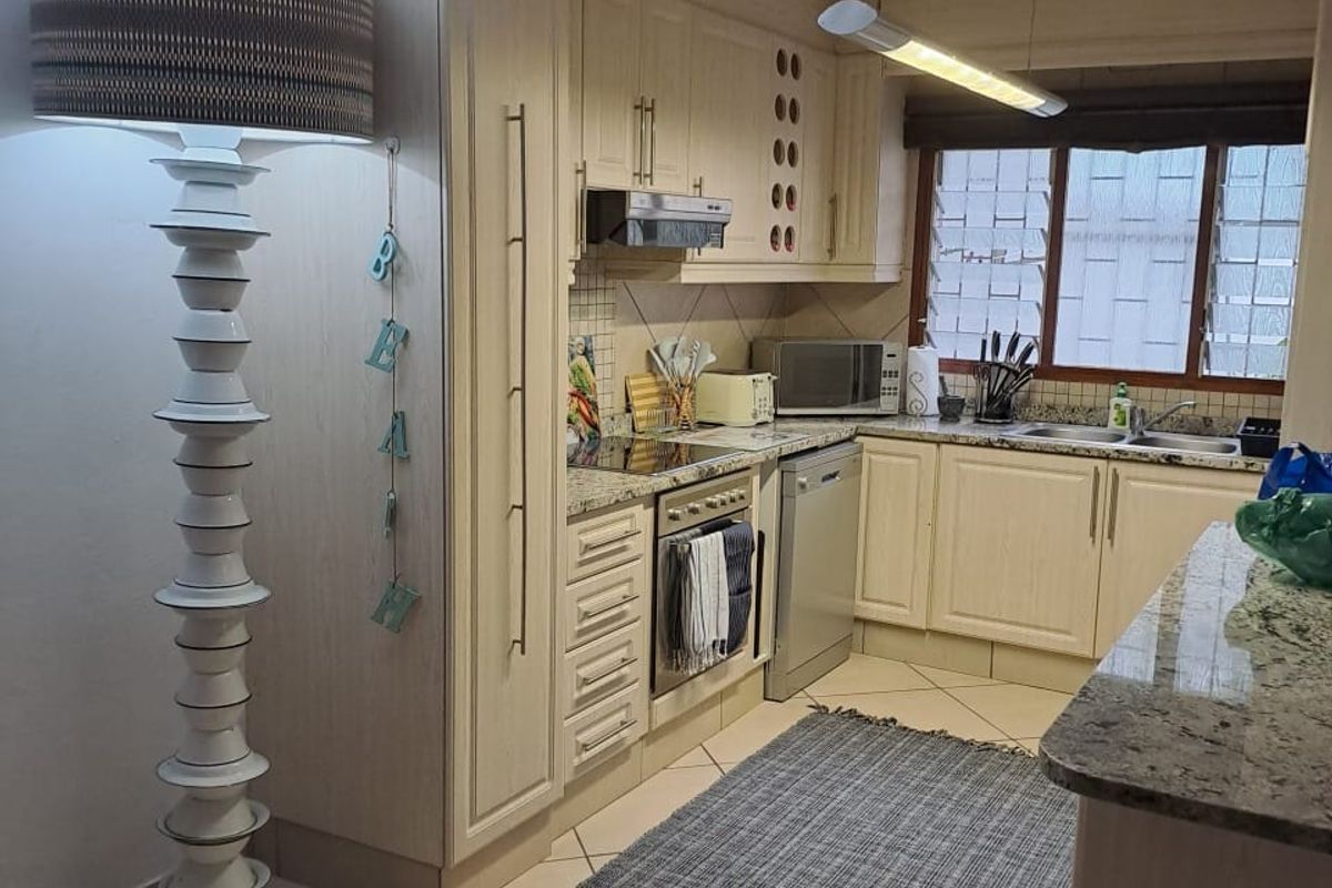 A functional kitchen featuring light-toned cabinetry, granite countertops, a built-in oven with extractor fan, and a double basin sink.