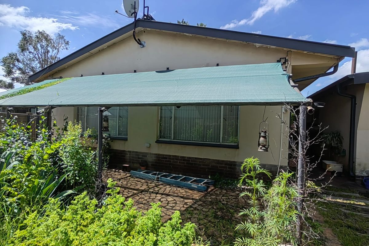Rear exterior view featuring a paved patio area with a shade cloth awning, brick base detailing, and security bars on the windows.
