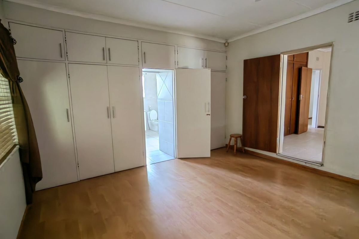 A spacious, empty bedroom featuring extensive built-in cupboards, laminate flooring, and direct access to an en-suite bathroom.