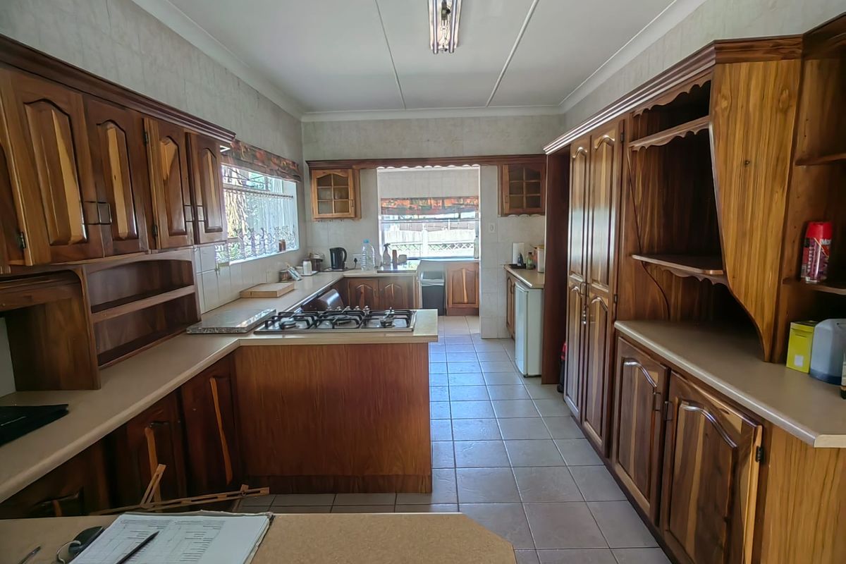 A functional kitchen featuring extensive built-in wooden cabinetry, a gas hob, and tiled flooring, offering a traditional layout with ample storage space.