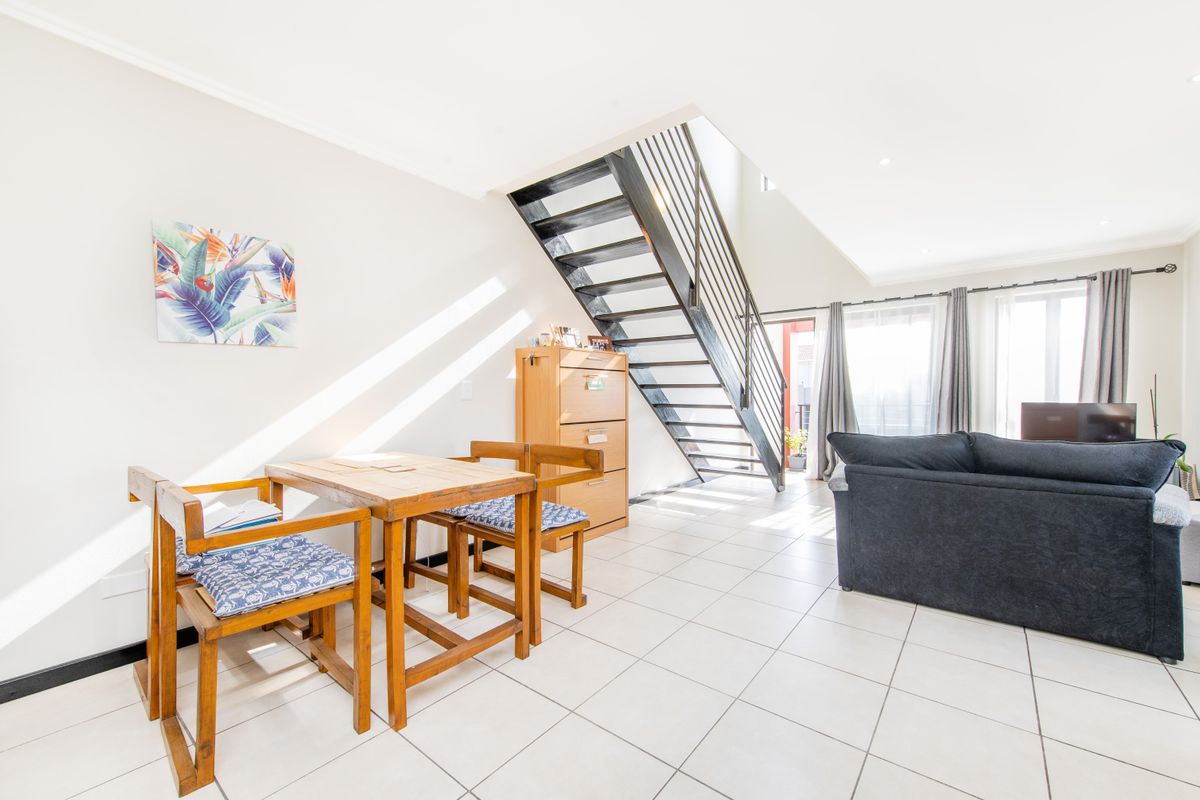 Open-plan living and dining area featuring tiled flooring, a modern metal staircase, and direct access to an outdoor balcony.