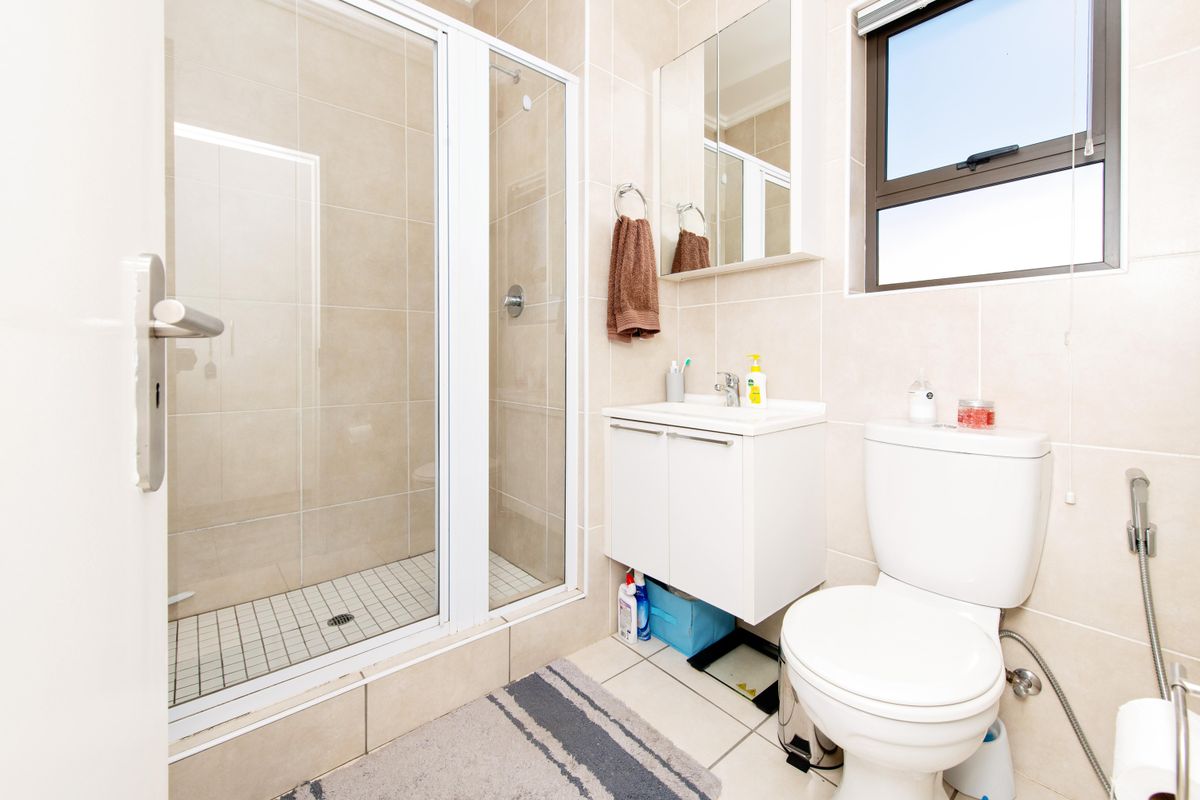 A clean, modern bathroom featuring a glass-enclosed shower, a wall-mounted vanity cabinet with a basin, and a standard toilet.