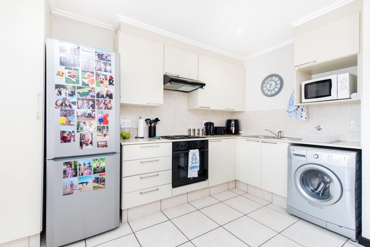 A functional kitchen featuring cream cabinetry, tiled splashbacks, built-in oven with hob, extractor fan, and integrated space for a washing machine.