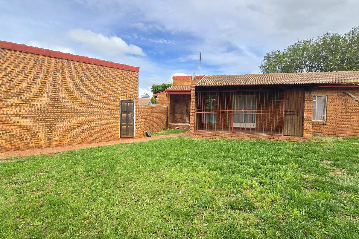 Rear view of a face brick house featuring a covered patio area with security gates, a paved walkway, and a spacious lawn.