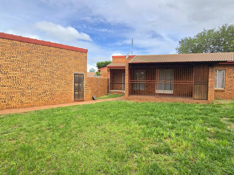 Rear view of a face brick house featuring a covered patio area with security gates, a paved walkway, and a spacious lawn.