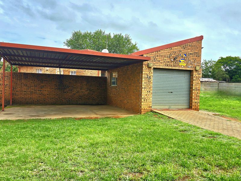 Front view of the property featuring a brick facade, a single roller garage door, and an attached carport with a paved driveway.