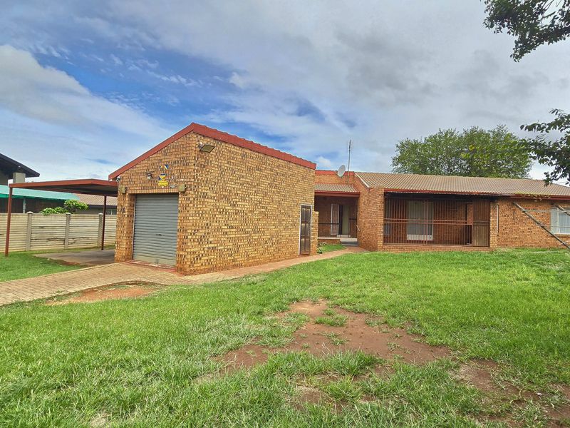 A single-story face brick house featuring a single garage, attached carport, and security bars on windows, set on a spacious grassed lot.