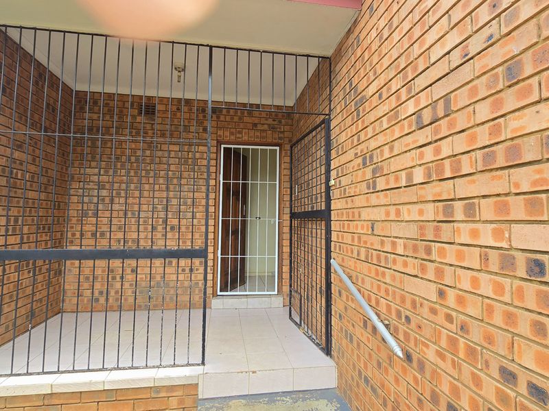 A secure entrance area featuring face brick walls, tiled flooring, and a protective metal security gate.