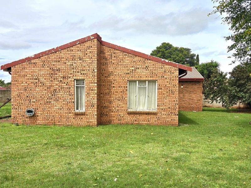 Rear view of a face brick house featuring a pitched roof, aluminium window frames, and a spacious surrounding lawn.