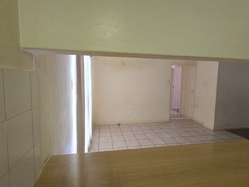An open-plan living area featuring tiled flooring and a kitchen pass-through counter, leading to a secondary space secured by a metal gate.