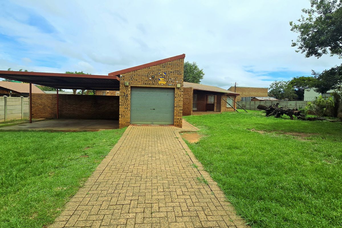 Front view of a brick house featuring a single garage, attached carport, paved driveway, and a large front garden area.