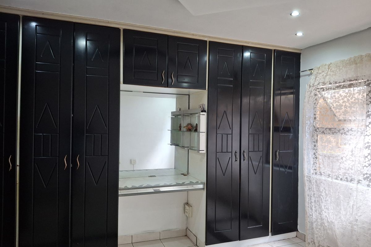 A bedroom featuring extensive dark built-in cabinetry with an integrated vanity area, recessed ceiling lighting, and tiled flooring.