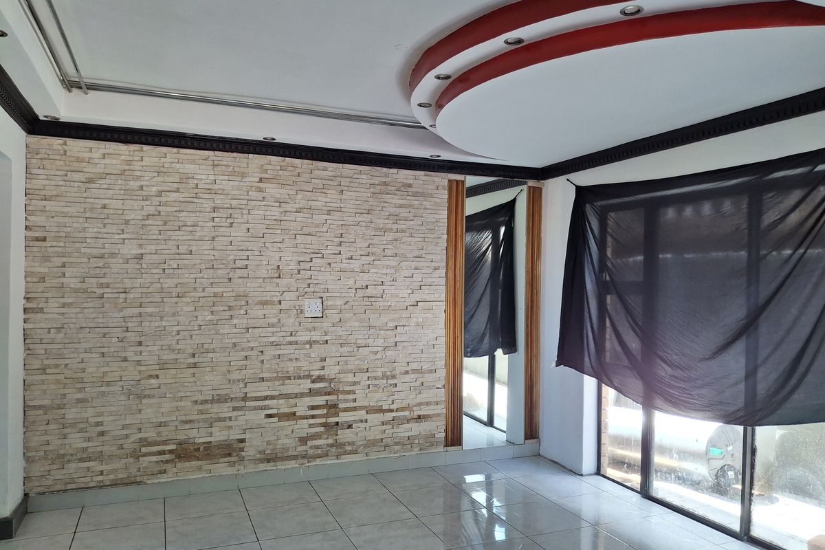 Empty living room featuring a stone veneer accent wall, tiled flooring, and a decorative recessed ceiling with integrated lighting.
