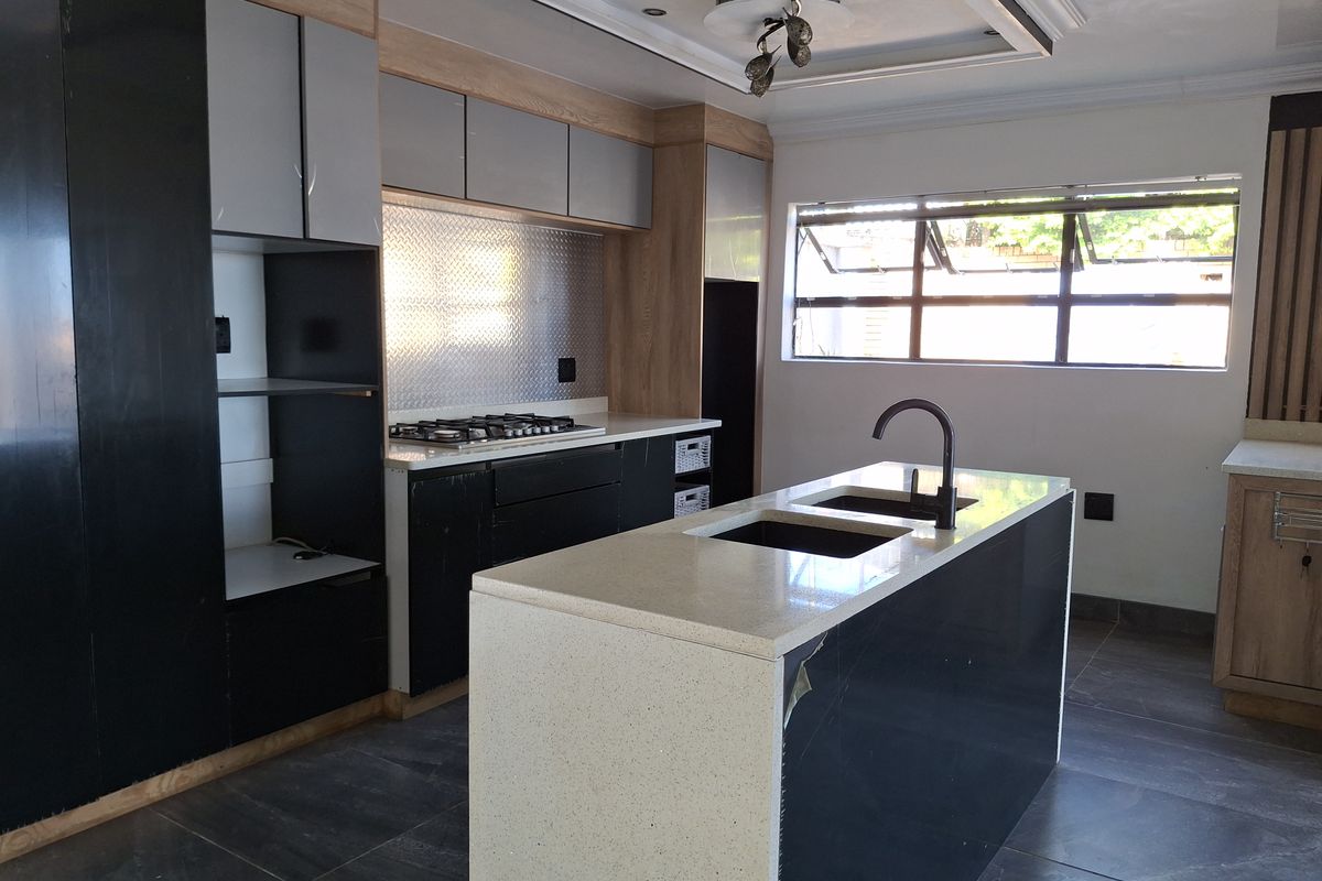 Modern kitchen featuring a central island with stone countertops, gas hob, double sink, and contemporary two-tone cabinetry with recessed ceiling lighting.