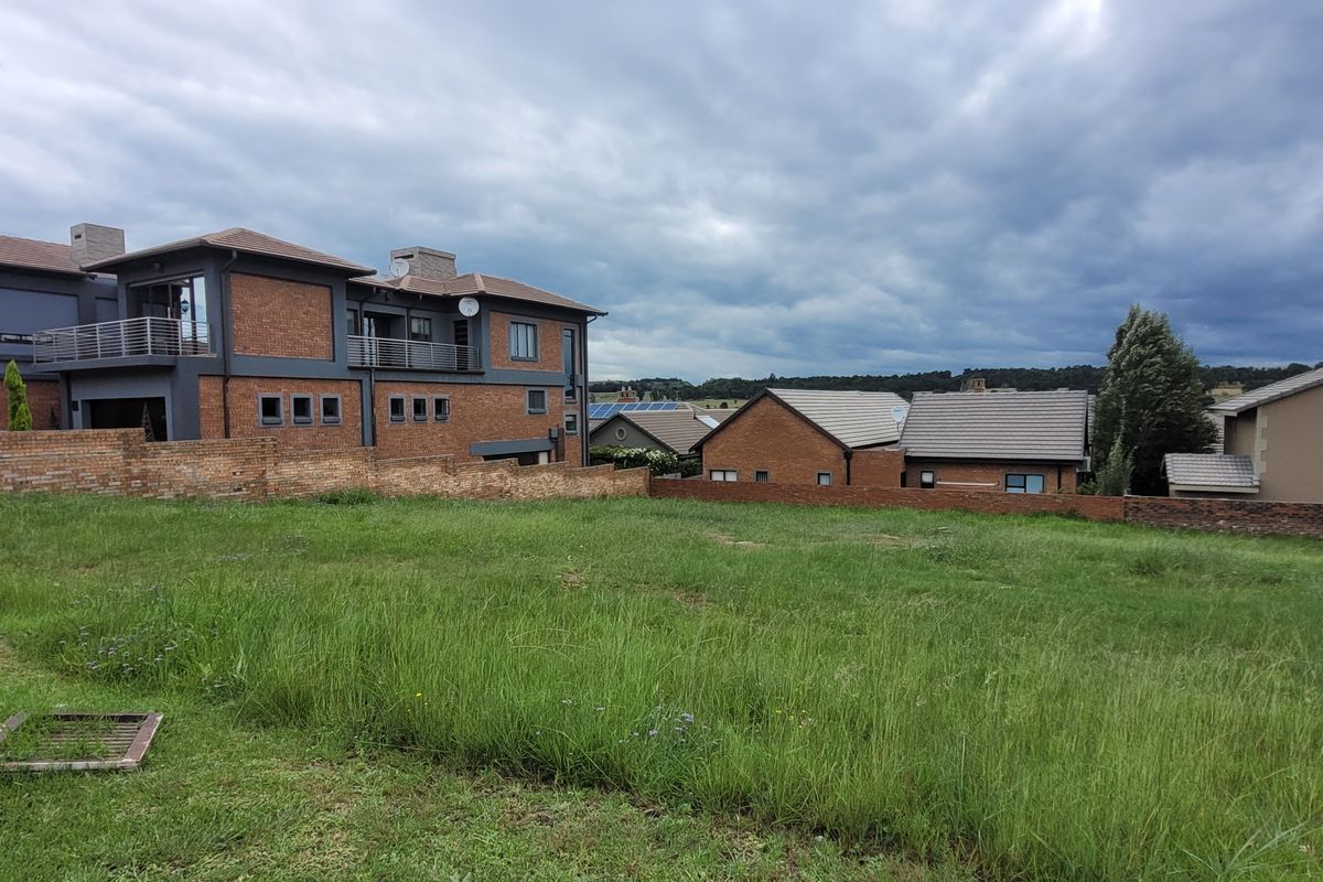 A vacant residential plot featuring a grass lawn and brick boundary wall, situated in a developed neighborhood with surrounding residential properties.