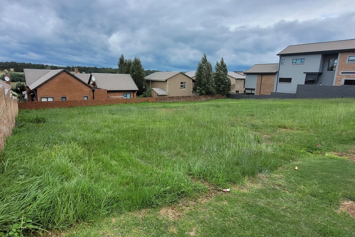A vacant residential plot featuring a grass lawn and brick boundary wall, situated within an established neighborhood.