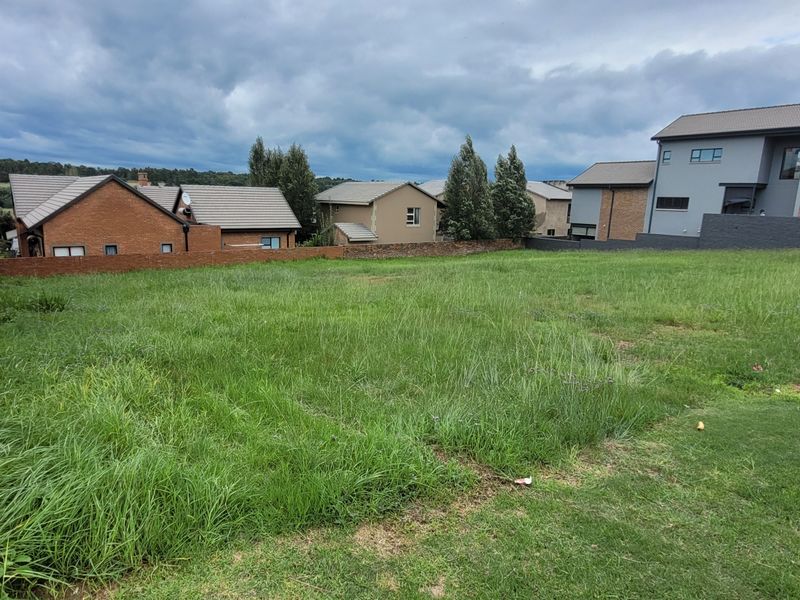 A vacant residential plot featuring a grass lawn and brick boundary wall, situated within an established neighborhood.