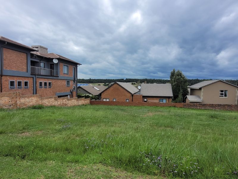 A vacant residential plot featuring a grassed surface and a brick boundary wall, situated in a developed neighborhood.