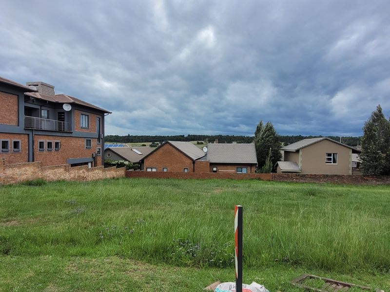 A vacant residential plot featuring a grass lawn and brick boundary wall, situated in a developed neighborhood with surrounding residential properties.