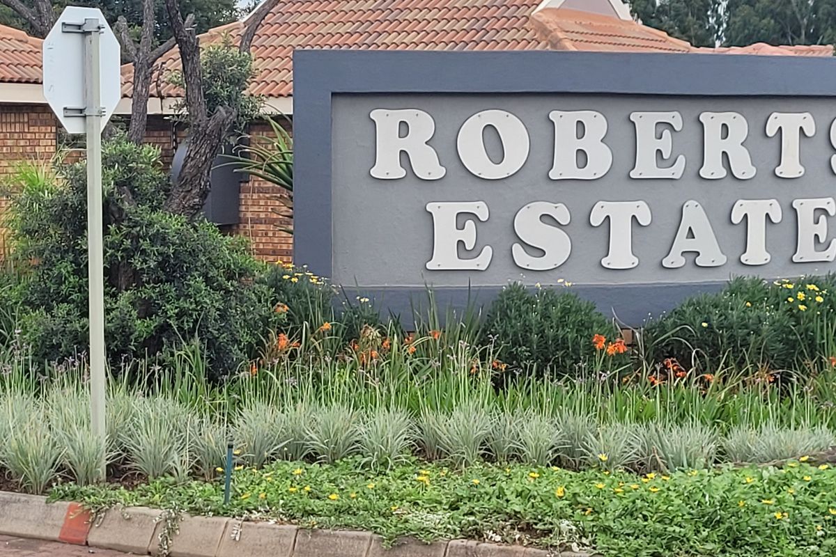 Entrance view of Roberts Estate featuring a prominent signage board, well-maintained landscaped garden, and brick boundary wall.