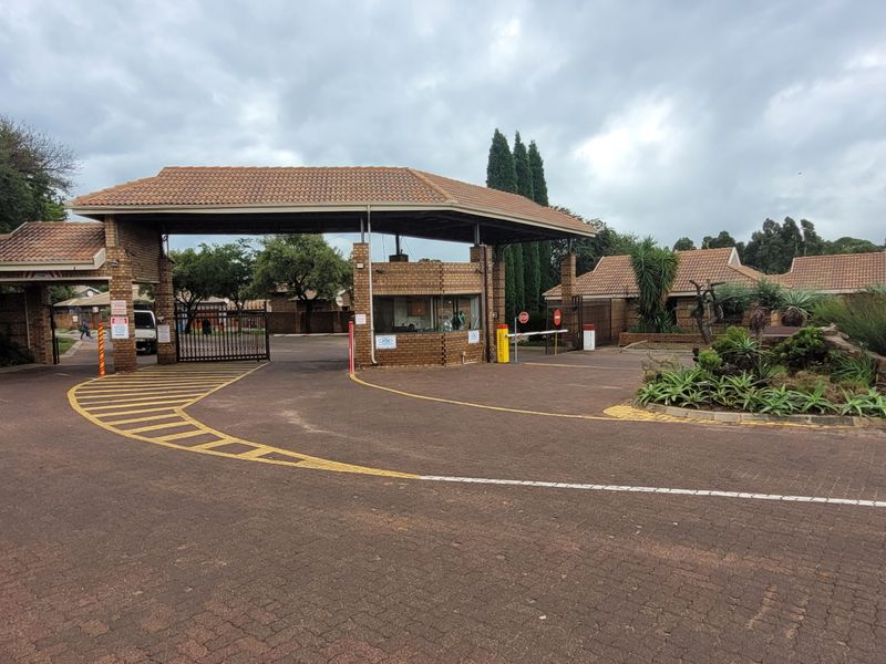 The main entrance to the residential estate featuring a secure gatehouse, paved driveway, and access control infrastructure.
