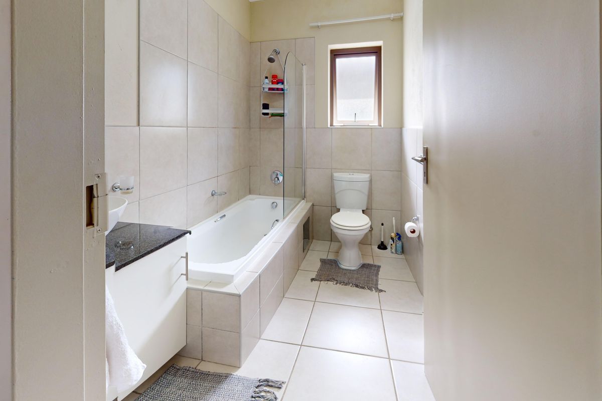A functional bathroom featuring a bathtub with a glass screen, a built-in vanity with a granite countertop, and neutral ceramic tiling throughout.