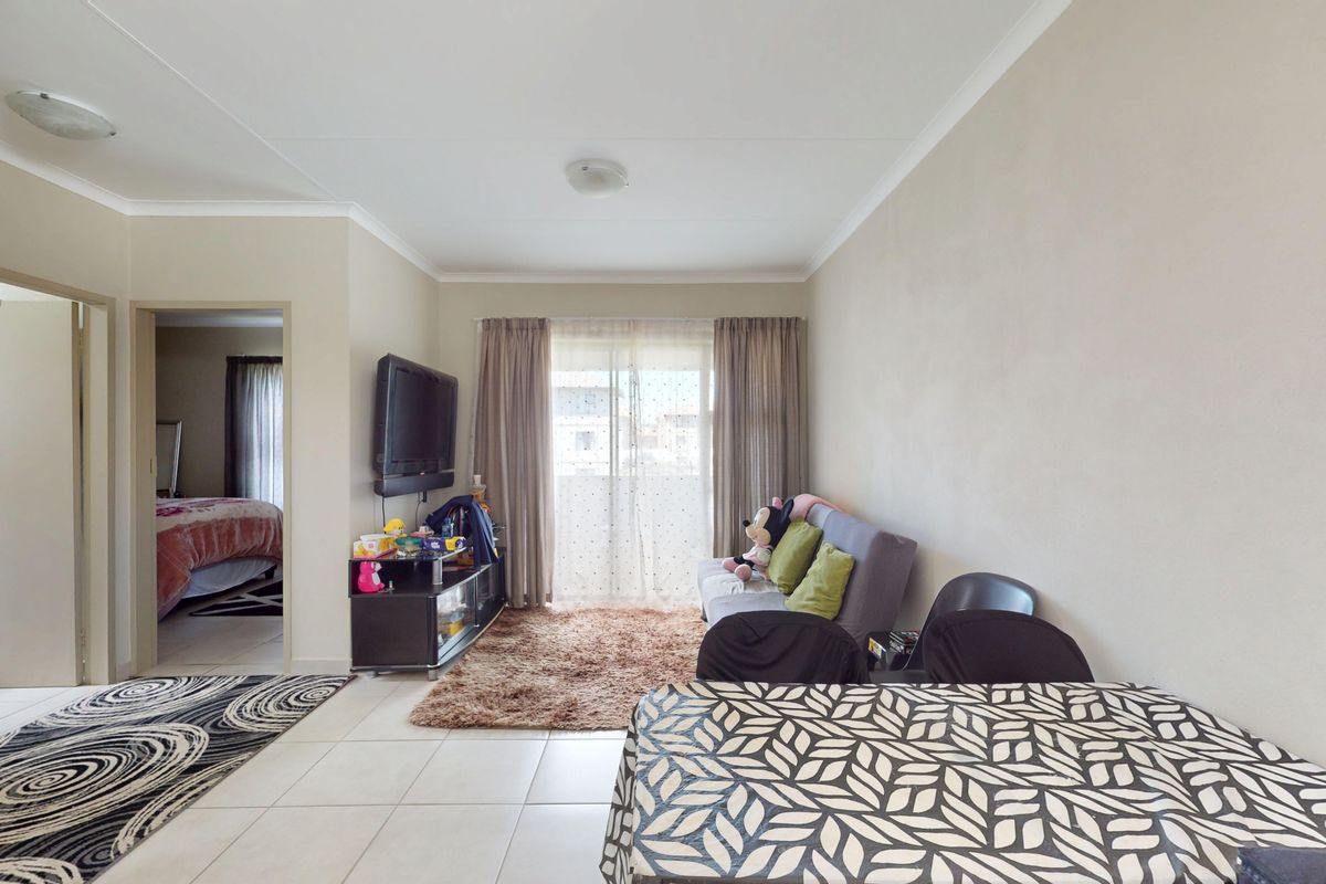 A bright living room featuring tiled flooring, coved ceilings, and a sliding glass door providing access to the exterior.