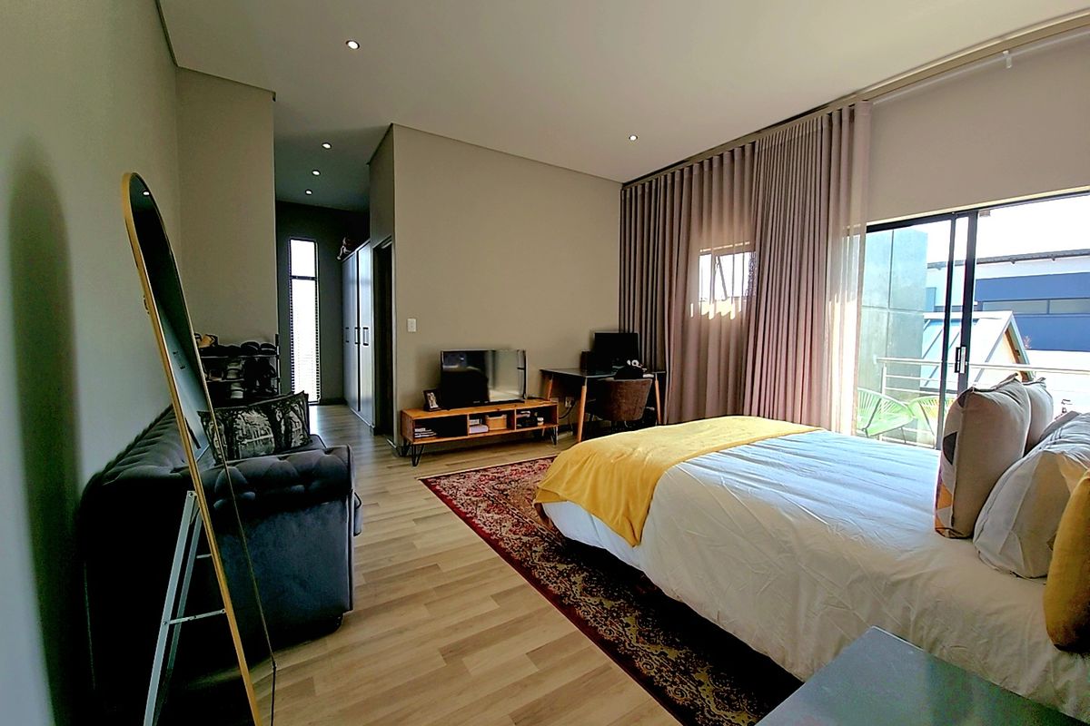 Spacious bedroom featuring modern laminate flooring, recessed lighting, and a large sliding glass door with floor-to-ceiling curtains providing access to an outdoor area.