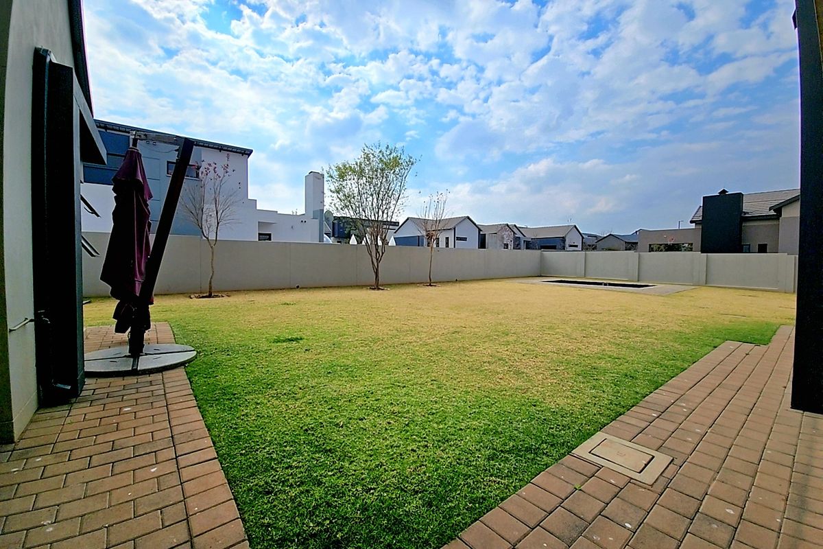 A spacious rear garden featuring a well-maintained lawn, paved patio area, perimeter walling, and a small plunge pool.