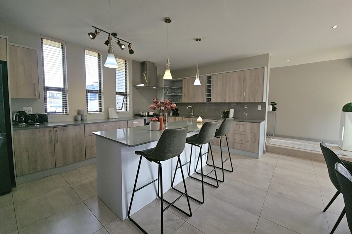 Modern open-plan kitchen featuring a central island with stone countertops, sleek wood-finish cabinetry, stainless steel extractor fan, and neutral tiled flooring.
