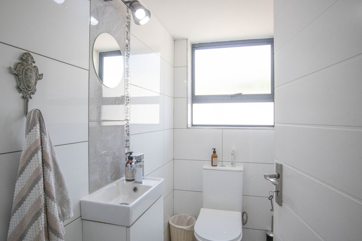 A modern, compact bathroom featuring white wall tiles, a sleek vanity basin with a mixer tap, and a standard toilet.