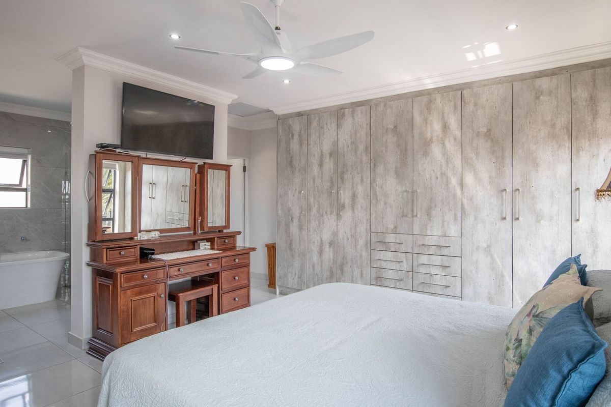 Spacious bedroom featuring extensive built-in cabinetry, modern ceiling fan, and an open-plan en-suite bathroom with a freestanding bathtub.