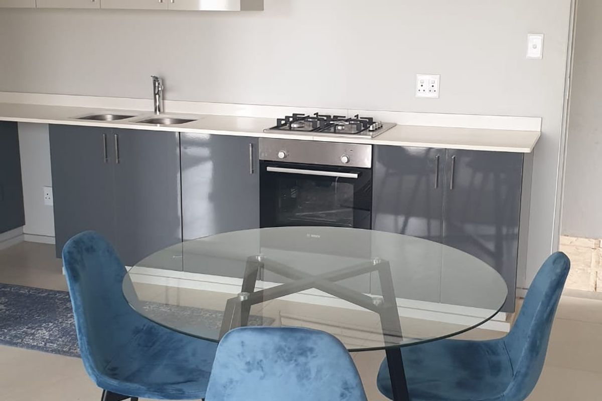 Modern kitchen featuring sleek grey cabinetry, built-in gas hob, oven, and stainless steel sink with neutral tiled flooring.