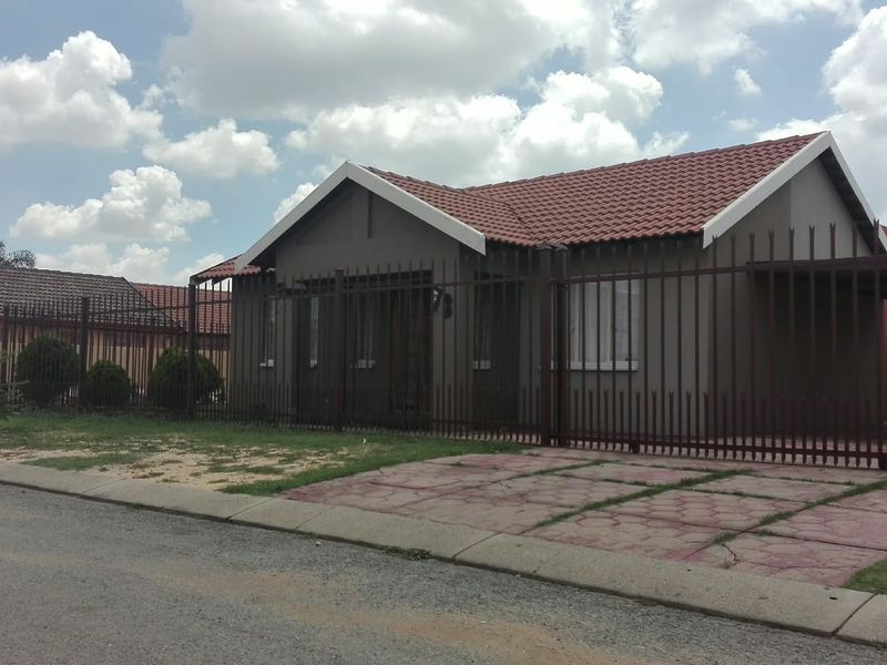 Front view of a single-story residential house featuring a tiled roof, paved driveway, and secure perimeter steel fencing.