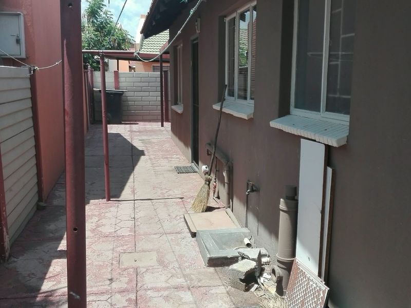 A narrow rear exterior walkway featuring paved flooring, precast boundary walls, and basic utility infrastructure along the side of the house.