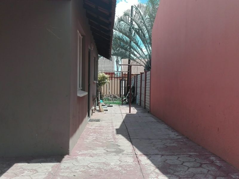 A narrow side passage featuring paved flooring and boundary walls, providing access to the rear of the property.