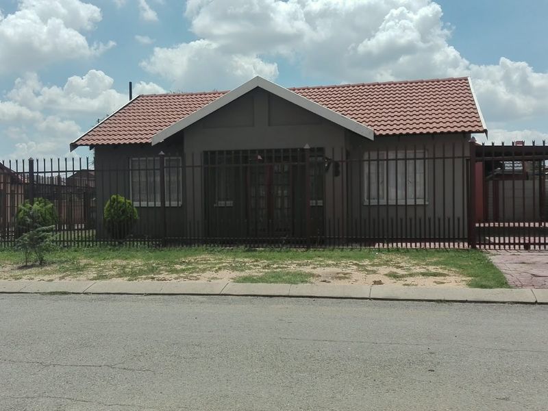 Front view of a single-story house featuring a tiled roof, secure perimeter fencing, and a paved driveway with an attached carport.