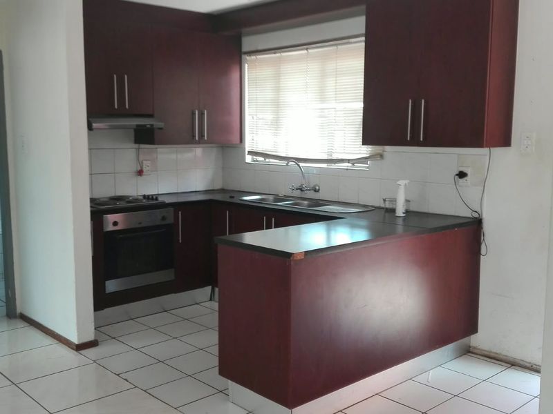 A functional kitchen featuring dark wood cabinetry, laminate countertops, built-in oven and hob, and tiled flooring, offering a clean space ready for updates.