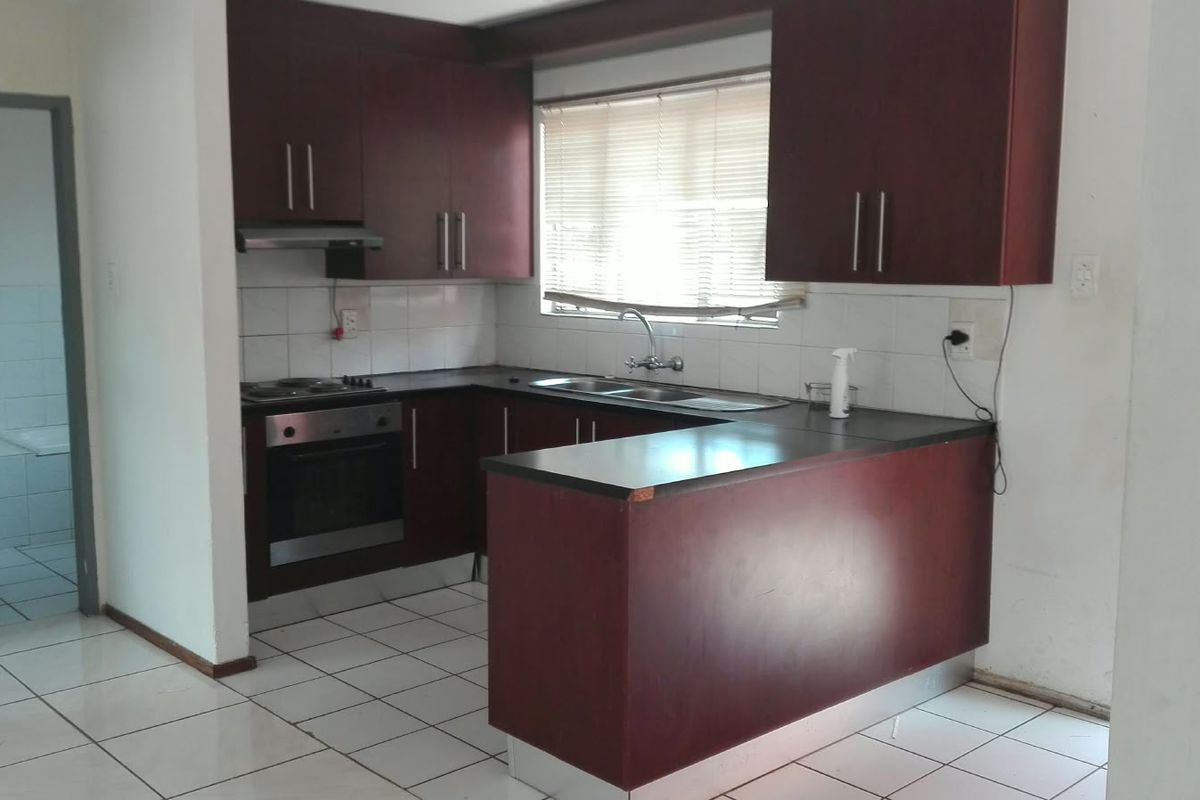 A functional kitchen featuring dark wood cabinetry, laminate countertops, built-in oven and hob, and tiled flooring, offering a clean space ready for updates.