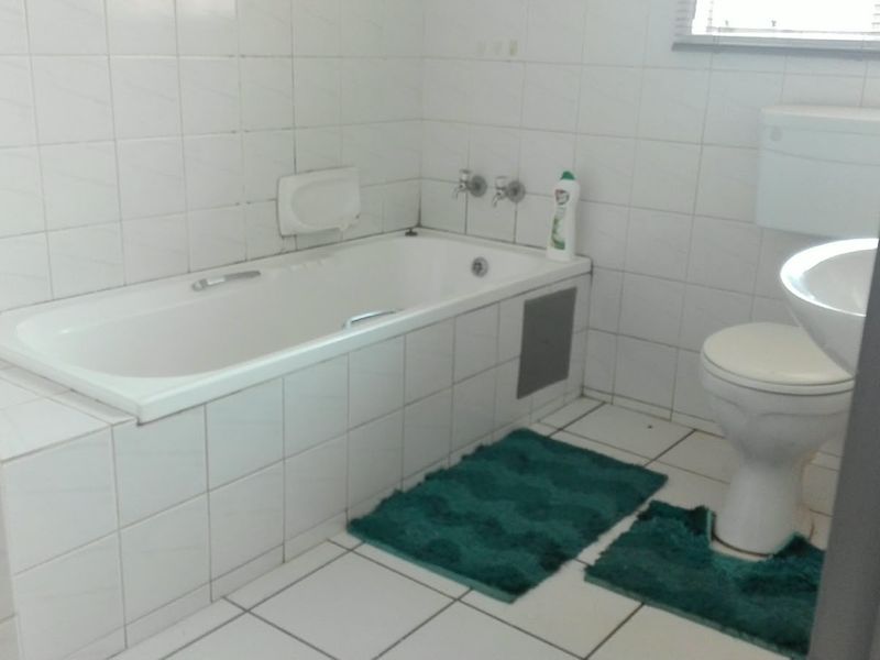 A dated bathroom featuring a built-in bathtub, pedestal basin, and toilet with white ceramic wall and floor tiles.