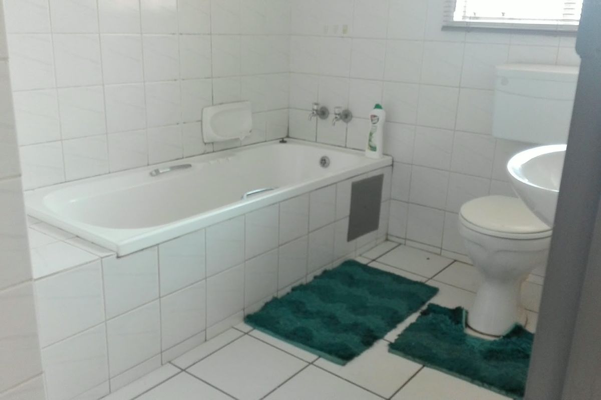 A dated bathroom featuring a built-in bathtub, pedestal basin, and toilet with white ceramic wall and floor tiles.