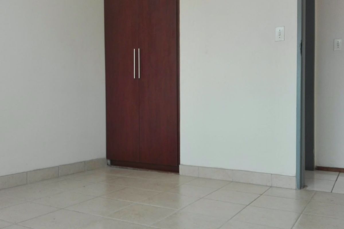 An empty bedroom featuring tiled flooring and a built-in wooden wardrobe with modern handles.