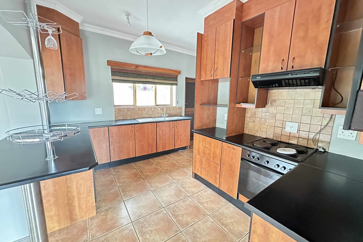 A functional kitchen featuring wood-tone cabinetry, dark countertops, a built-in oven with extractor fan, and tiled flooring.
